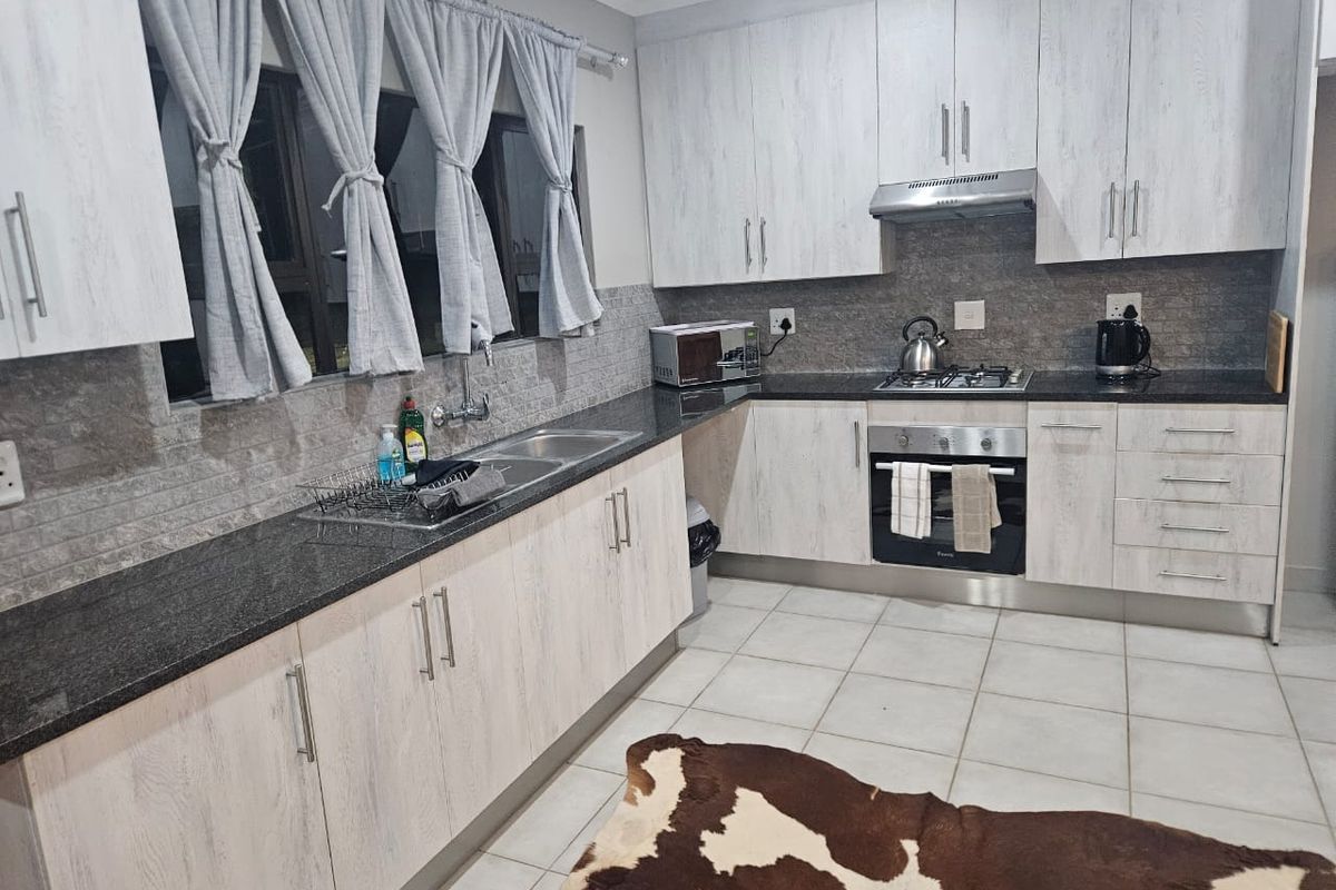 Modern kitchen featuring light wood-grain cabinetry, dark granite countertops, stainless steel appliances, and a tiled backsplash.