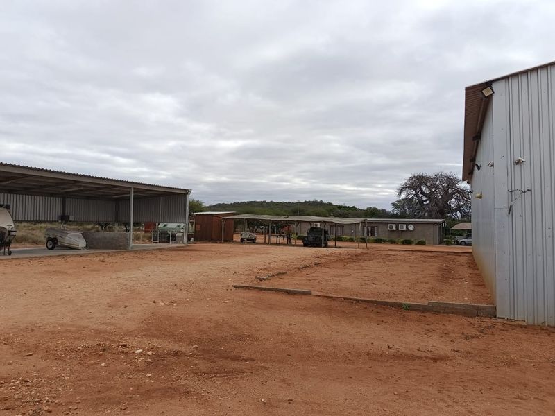 Spacious farm yard featuring a large corrugated metal shed, open-sided carport structure, and expansive unpaved ground area suitable for agricultural or storage use.