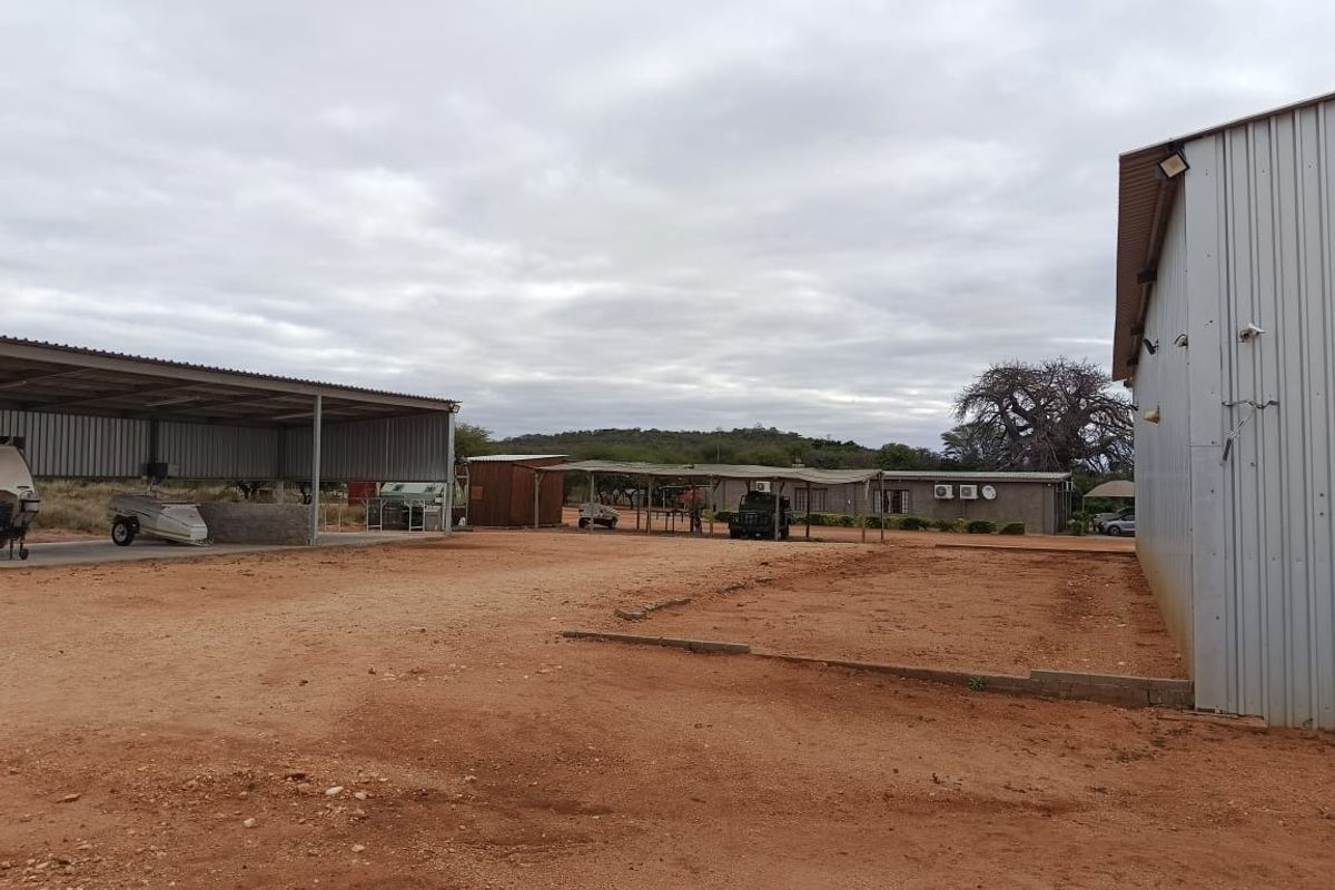 Spacious farm yard featuring a large corrugated metal shed, open-sided carport structure, and expansive unpaved ground area suitable for agricultural or storage use.