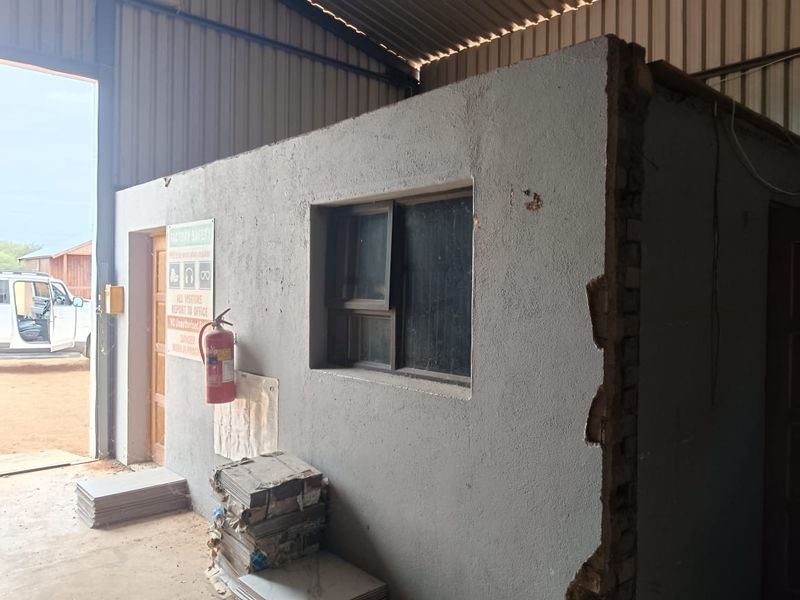 An industrial utility space or workshop area featuring exposed brickwork, a fire extinguisher, and an aluminium window frame within a large shed structure.