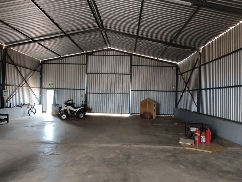 A spacious, high-ceilinged industrial garage or storage shed featuring corrugated metal walls, exposed steel trusses, and durable concrete flooring.