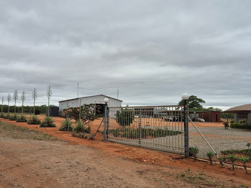 Front entrance view of the farm property featuring a metal sliding gate, electric fencing, and a large industrial shed structure on a gravel driveway.
