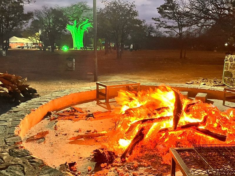 An outdoor stone-clad fire pit area with integrated braai facilities, set within a natural farm landscape at night.