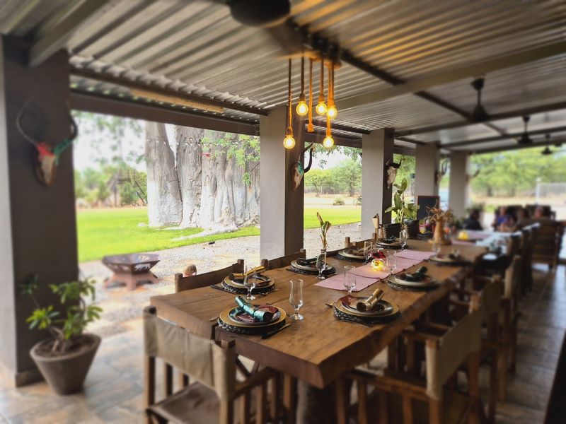 Spacious covered outdoor patio featuring a corrugated metal roof, concrete support pillars, and tiled flooring, overlooking a large garden area.