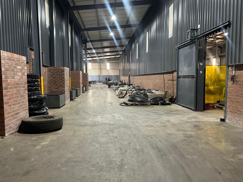 Spacious industrial warehouse unit featuring high ceilings, corrugated metal walls, concrete flooring, and large sliding access doors, suitable for storage or manufacturing operations.