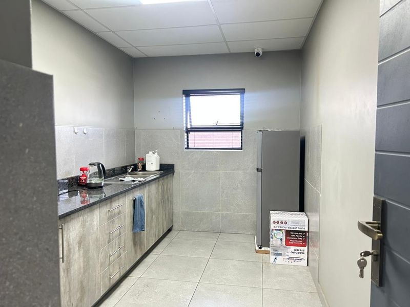 A functional kitchenette featuring granite countertops, tiled backsplash, tiled flooring, and a drop ceiling, suitable for office or commercial use.