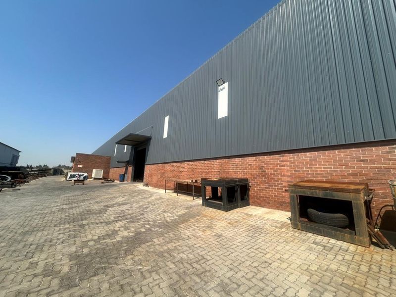 Rear exterior view of a commercial warehouse featuring corrugated metal cladding, face brick base, and a paved yard area.