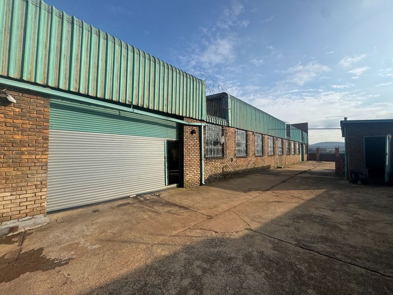 Rear industrial yard featuring a large roller shutter door, brick facade, and secure perimeter fencing with razor wire.