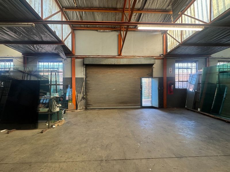 Spacious industrial utility area featuring high ceilings with exposed steel trusses, concrete flooring, and a large roller shutter door for vehicle or equipment access.