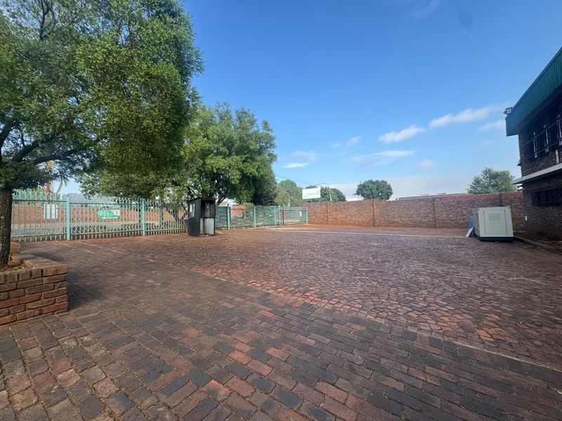 A secure industrial yard featuring brick paving, perimeter walling, security fencing, and a dedicated guard booth with an installed generator.