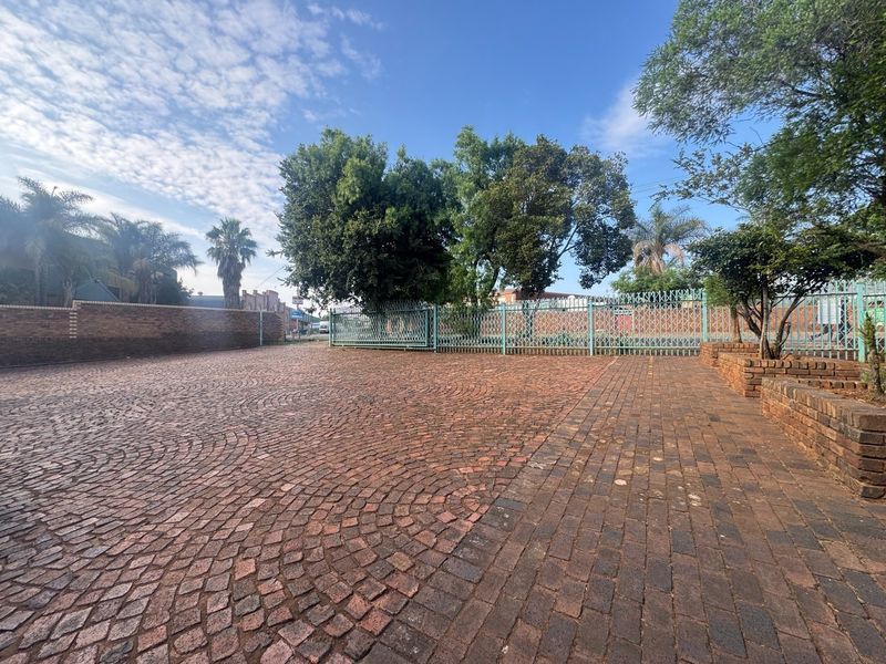 A spacious industrial exterior area featuring durable cobblestone paving, secure metal fencing, and established brick boundary walls.