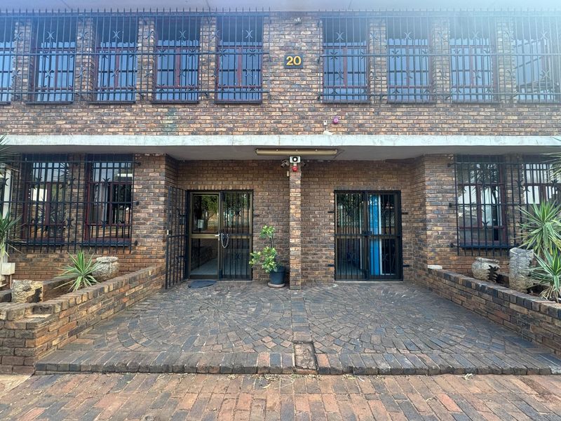 Front facade of an industrial building featuring face brick construction, secure metal window bars, and a paved entrance area with dual access points.