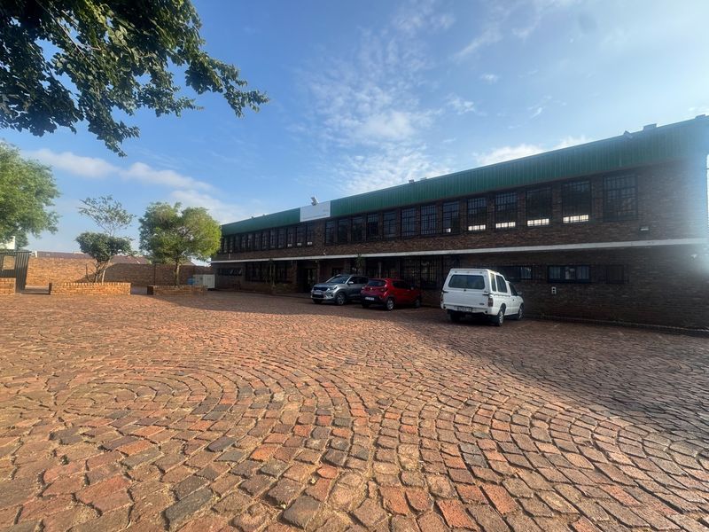 Front exterior view of a two-story industrial face brick building featuring a large paved courtyard and secure window grilles.