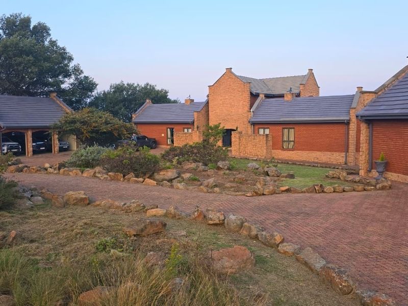 A spacious lodge-style property featuring a brick facade, tiled roof, and a large paved driveway leading to a triple garage.