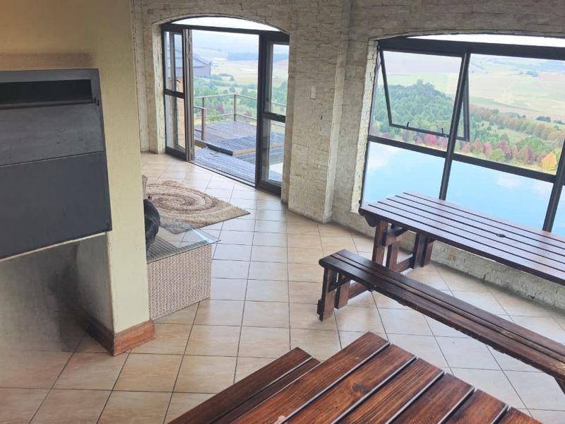 Spacious covered patio featuring a built-in fireplace, tiled flooring, and expansive glass windows offering panoramic landscape views.