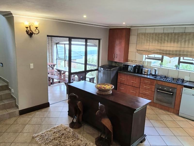 A functional kitchen featuring wooden cabinetry, built-in appliances, tiled flooring, and a stone feature wall, with direct access to an outdoor patio area.