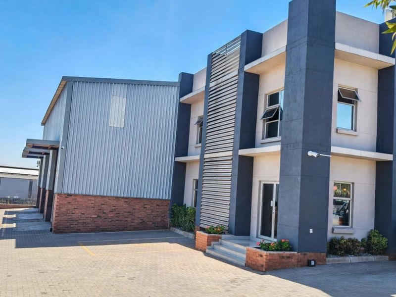 Modern office building exterior featuring a combination of brickwork, metal cladding, and paved parking area with integrated security features.