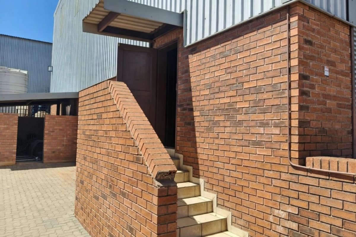 Exterior view of an industrial office building featuring a brick staircase leading to an elevated entrance with metal cladding and paved ground area.