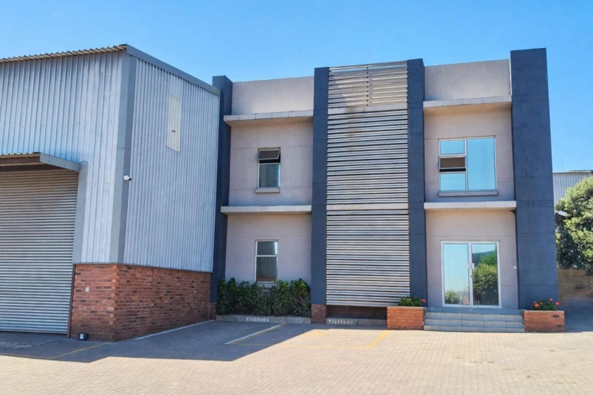 Modern office building exterior featuring a combination of brick, metal cladding, and glass, with a dedicated paved parking area and visitor bays.