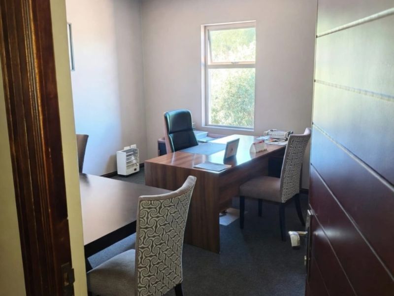 A functional office space featuring carpeted flooring, a suspended ceiling with recessed lighting, and a window providing natural light.
