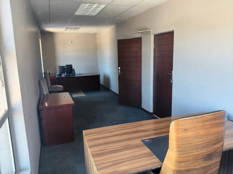 A functional office space featuring carpeted flooring, suspended ceiling tiles, and two solid core doors, providing a professional work environment.