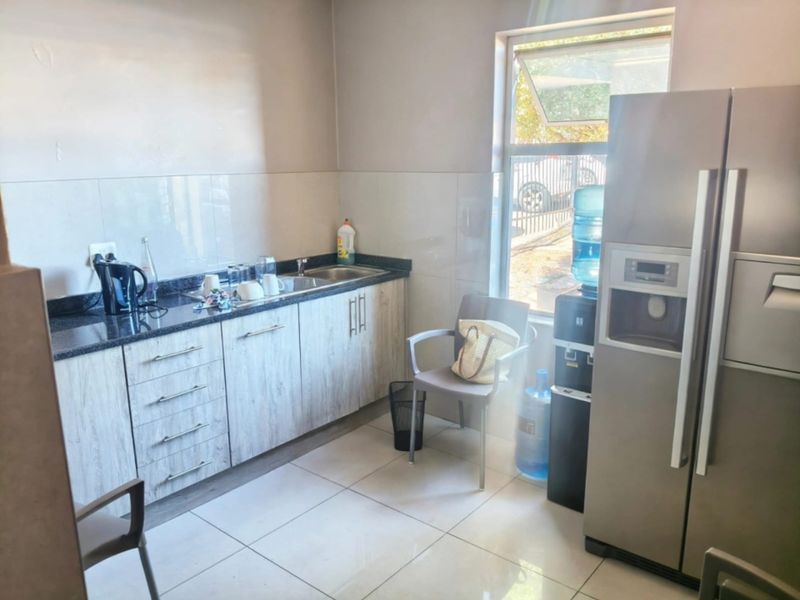 A functional office kitchenette featuring granite countertops, built-in cabinetry, a stainless steel sink, and tiled flooring with natural light from a side window.