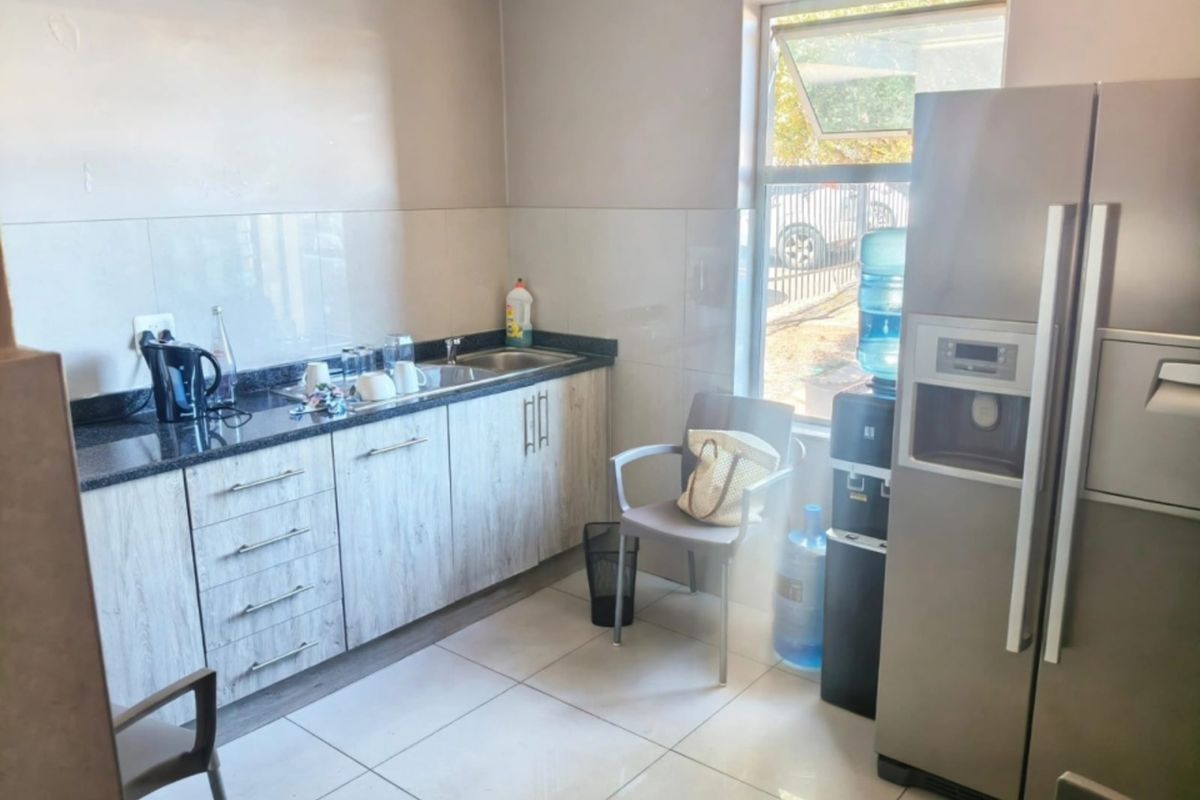 A functional office kitchenette featuring granite countertops, built-in cabinetry, a stainless steel sink, and tiled flooring with natural light from a side window.