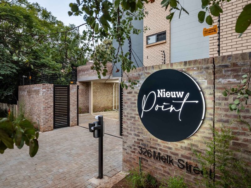Front entrance view of Nieuw Point apartment complex featuring a brick boundary wall, paved driveway, and secure gated access.