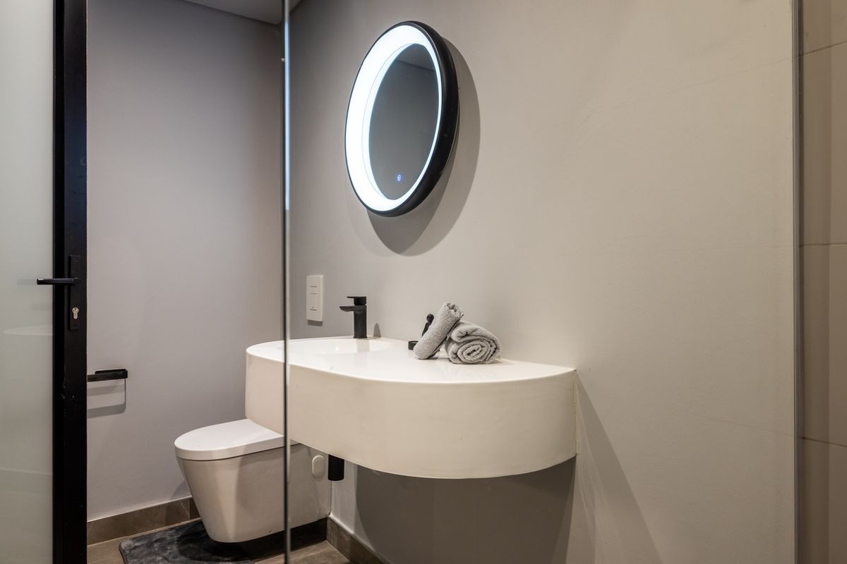 Modern bathroom featuring a sleek wall-mounted vanity, black fixtures, a contemporary back-to-wall toilet, and a stylish LED backlit circular mirror.