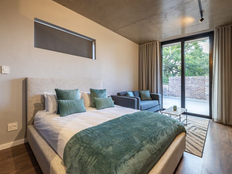 Modern bedroom featuring an exposed concrete ceiling, laminate flooring, and a large sliding glass door providing access to an outdoor area.