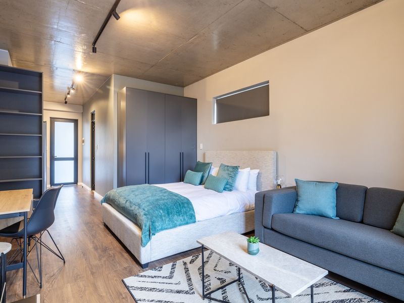 Modern open-plan studio apartment featuring an exposed concrete ceiling, sleek built-in cabinetry, and high-quality laminate flooring in a contemporary urban setting.