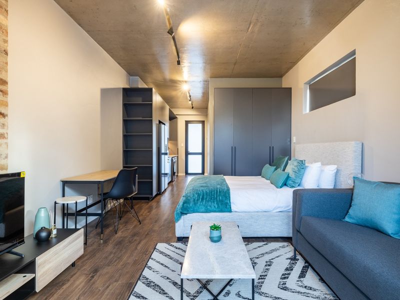 Modern open-plan studio apartment featuring an exposed concrete ceiling, brick accent wall, sleek built-in cabinetry, and high-quality laminate flooring.