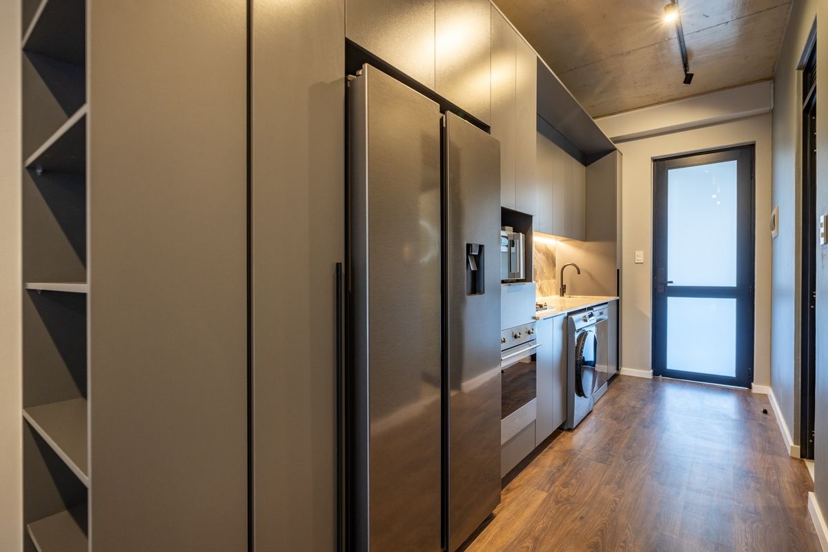 Modern galley-style kitchen featuring sleek grey cabinetry, integrated appliances, stone countertops, and an industrial-style exposed concrete ceiling.