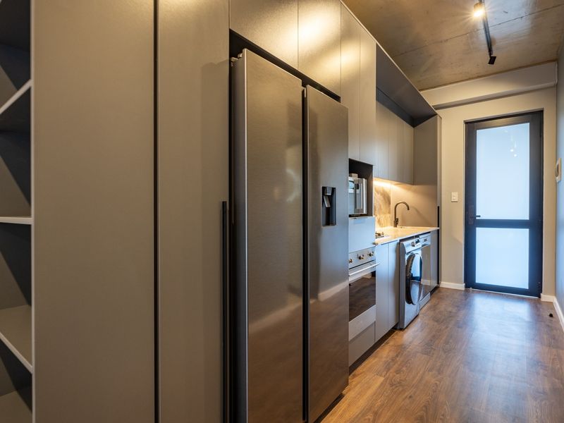 Modern galley-style kitchen featuring sleek grey cabinetry, integrated appliances, stone countertops, and an industrial-style exposed concrete ceiling.