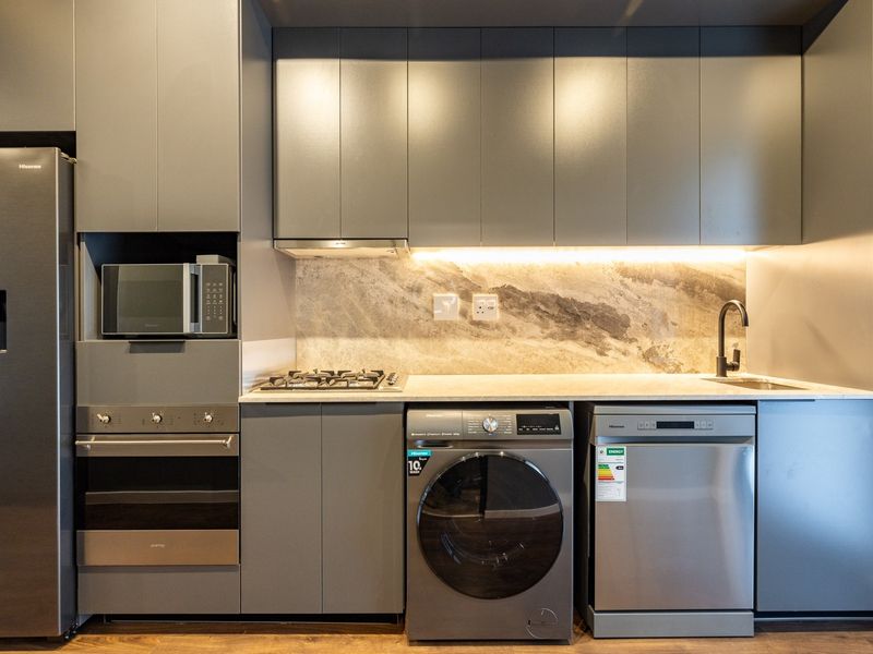 Modern kitchen featuring sleek grey cabinetry, stone countertops, integrated appliances, and under-cabinet lighting for a clean, contemporary aesthetic.
