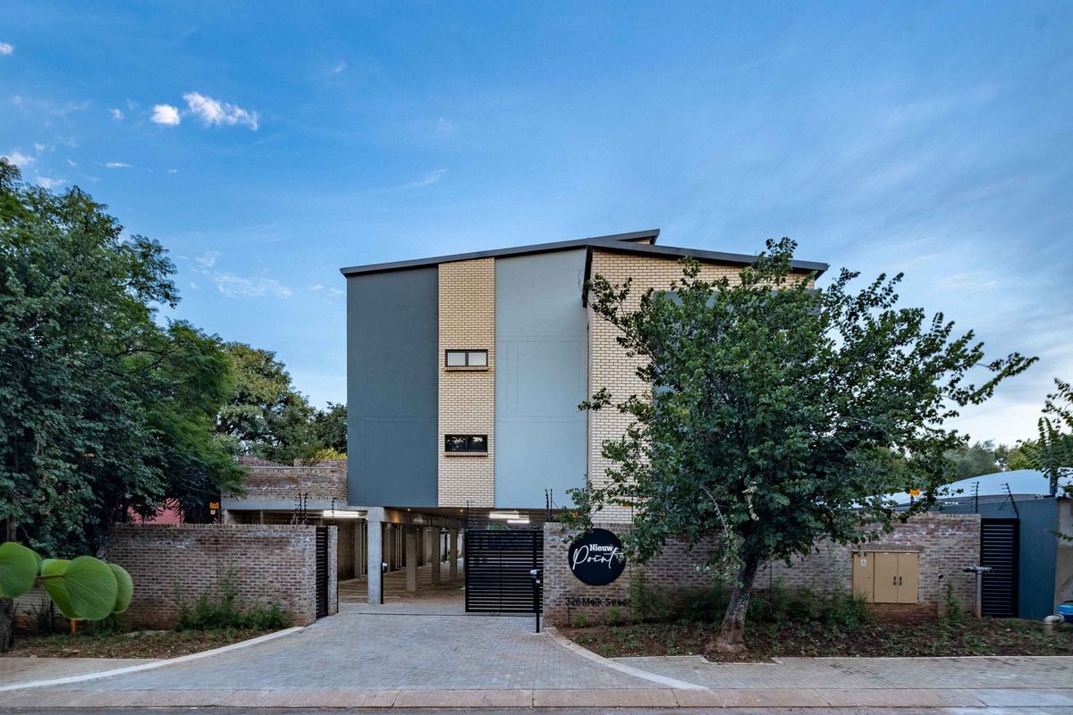 Front elevation of the apartment complex featuring a modern facebrick facade, secure gated entrance, paved driveway, and perimeter electric fencing.