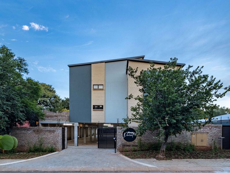 Front elevation of the apartment complex featuring a modern facebrick facade, secure gated entrance, paved driveway, and perimeter electric fencing.