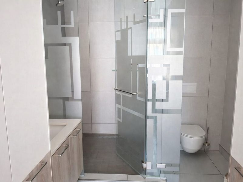 Modern bathroom featuring a walk-in shower with decorative frosted glass, a wall-hung toilet, and a sleek vanity cabinet with an integrated basin.