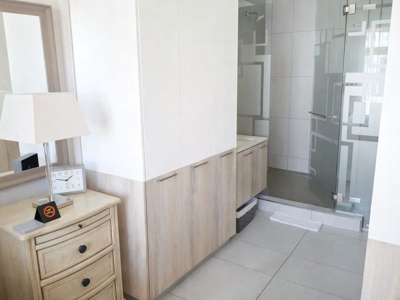 Modern bathroom featuring built-in cabinetry, a glass-enclosed shower, and neutral tiled finishes, offering a clean and functional space.