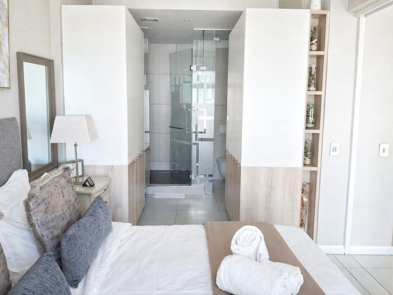 Modern bedroom featuring built-in cupboards and a sleek en-suite bathroom with a glass-enclosed shower.