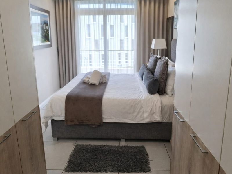 A well-maintained bedroom featuring built-in cupboards, tiled flooring, and direct access to a balcony through a sliding glass door.