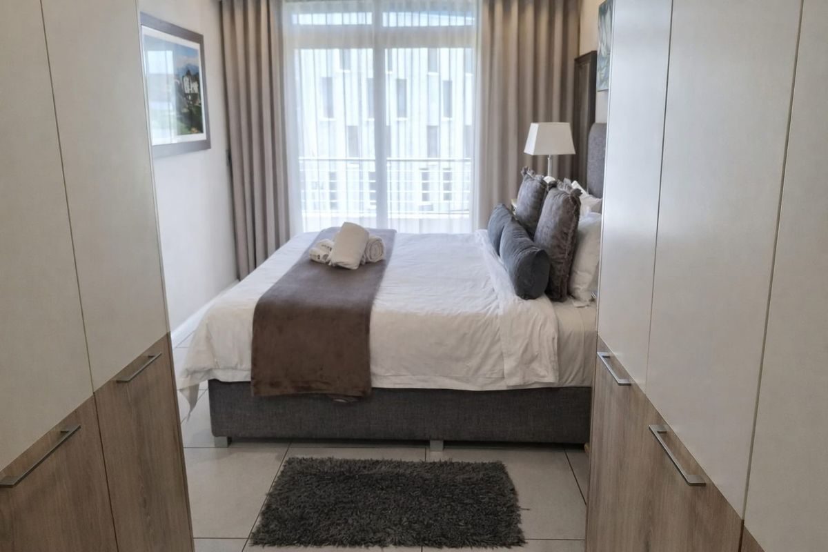 A well-maintained bedroom featuring built-in cupboards, tiled flooring, and direct access to a balcony through a sliding glass door.