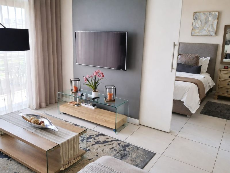 Open plan living area featuring tiled flooring and a feature wall, with direct access to a balcony and an adjacent bedroom.