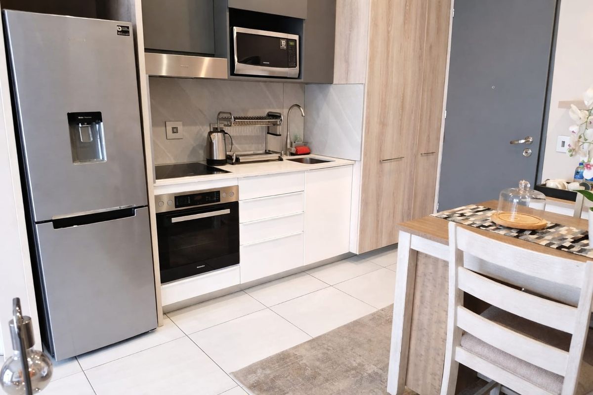 Modern compact kitchen featuring sleek white and wood-tone cabinetry, integrated appliances, a built-in oven, and a clean tiled floor finish.