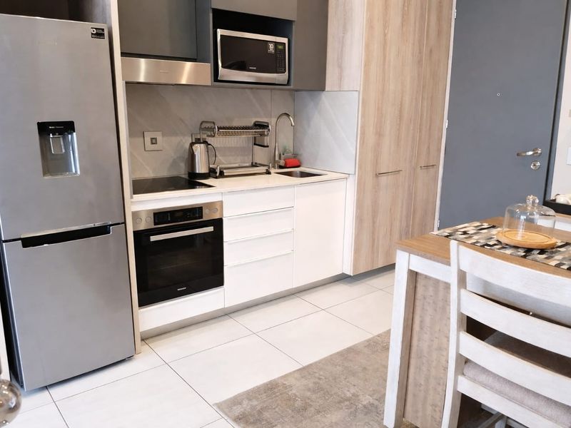 Modern compact kitchen featuring sleek white and wood-tone cabinetry, integrated appliances, a built-in oven, and a clean tiled floor finish.
