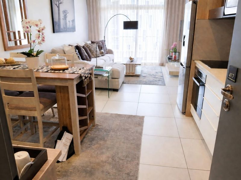Modern open-plan apartment featuring a compact kitchen with built-in appliances, tiled flooring, and a bright living area leading to a balcony.