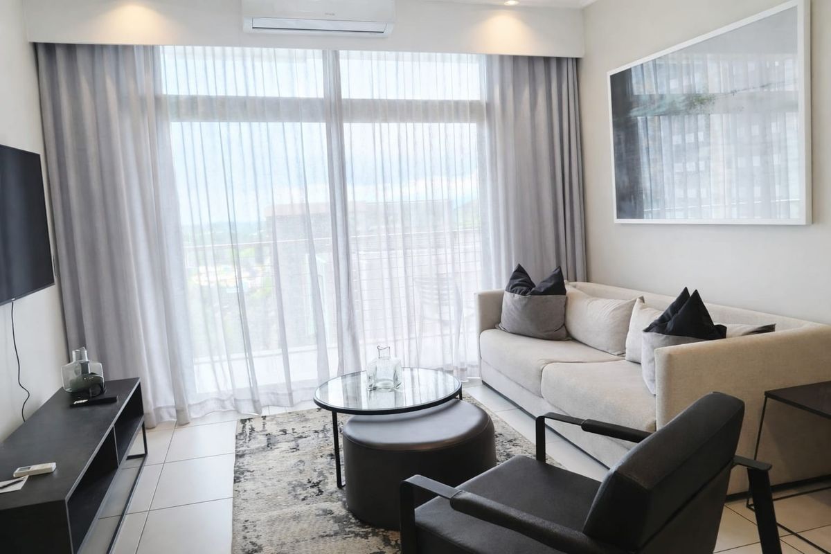 A modern, well-lit living room featuring tiled flooring, a split-system air conditioner, and large sliding glass doors leading to a balcony.
