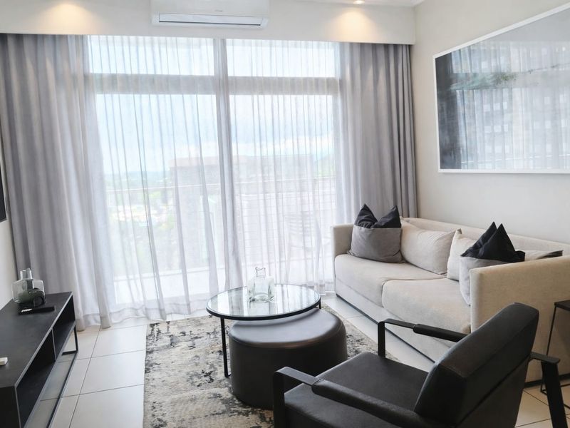A modern, well-lit living room featuring tiled flooring, a split-system air conditioner, and large sliding glass doors leading to a balcony.