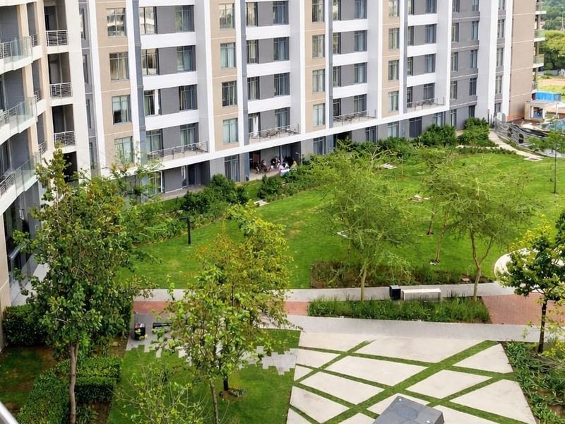 Elevated view of a well-maintained communal garden area featuring paved pathways, mature trees, and landscaped lawns between apartment building blocks.