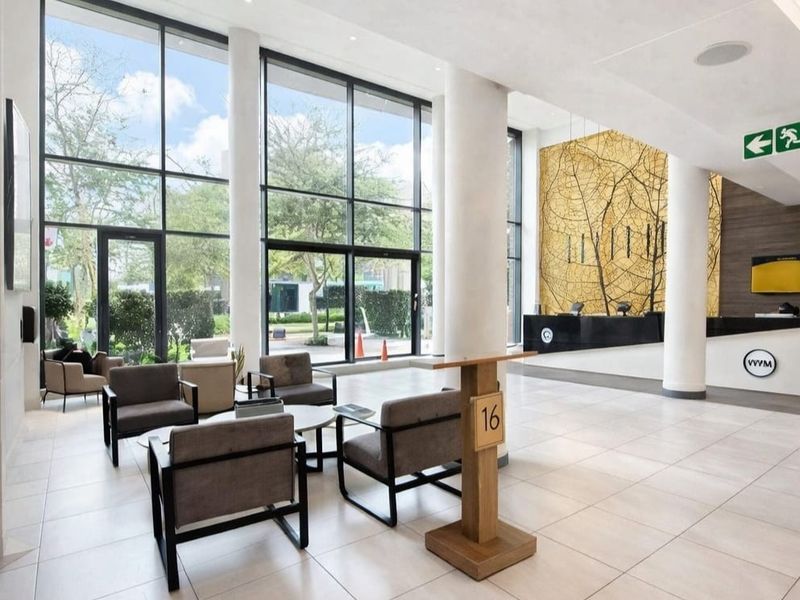 Modern apartment building lobby featuring high ceilings, floor-to-ceiling windows, tiled floors, and a professional reception area.